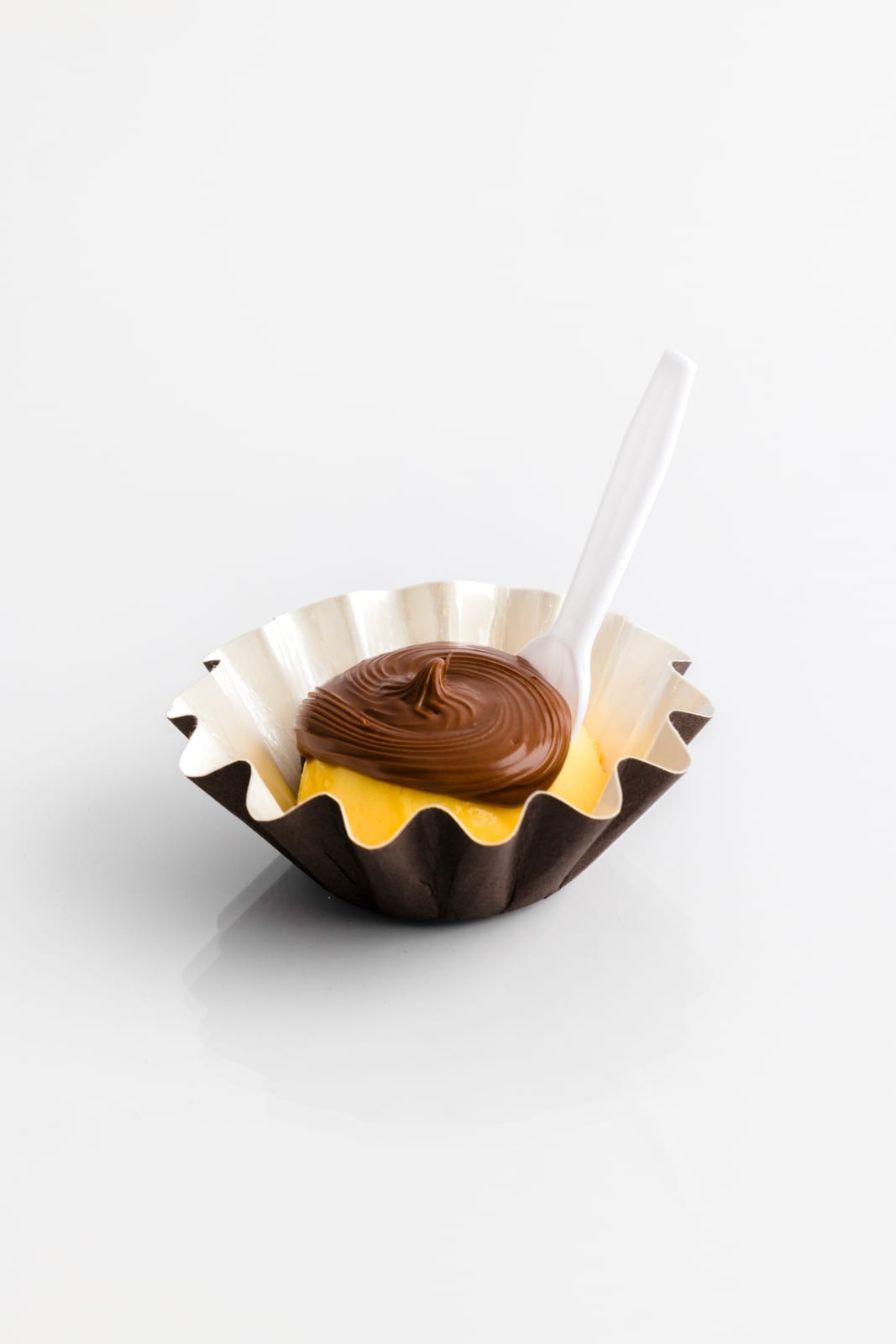 Mini flan in a fluted paper cup spread with a swirl of Nutella, a small white spoon resting inside